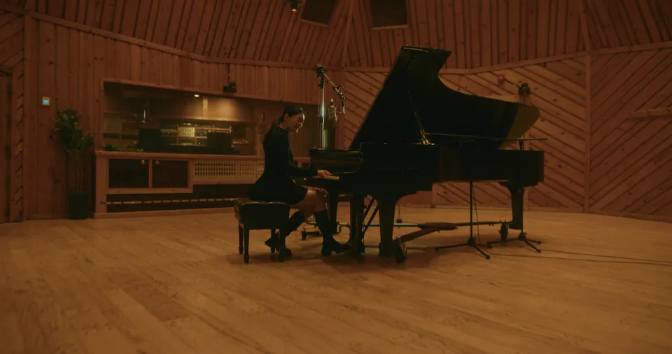 Music video still filmed at Power Station at BerkleeNYC in Hell’s Kitchen, NYC: the wood-paneled live room with a pianist at the Steinway grand