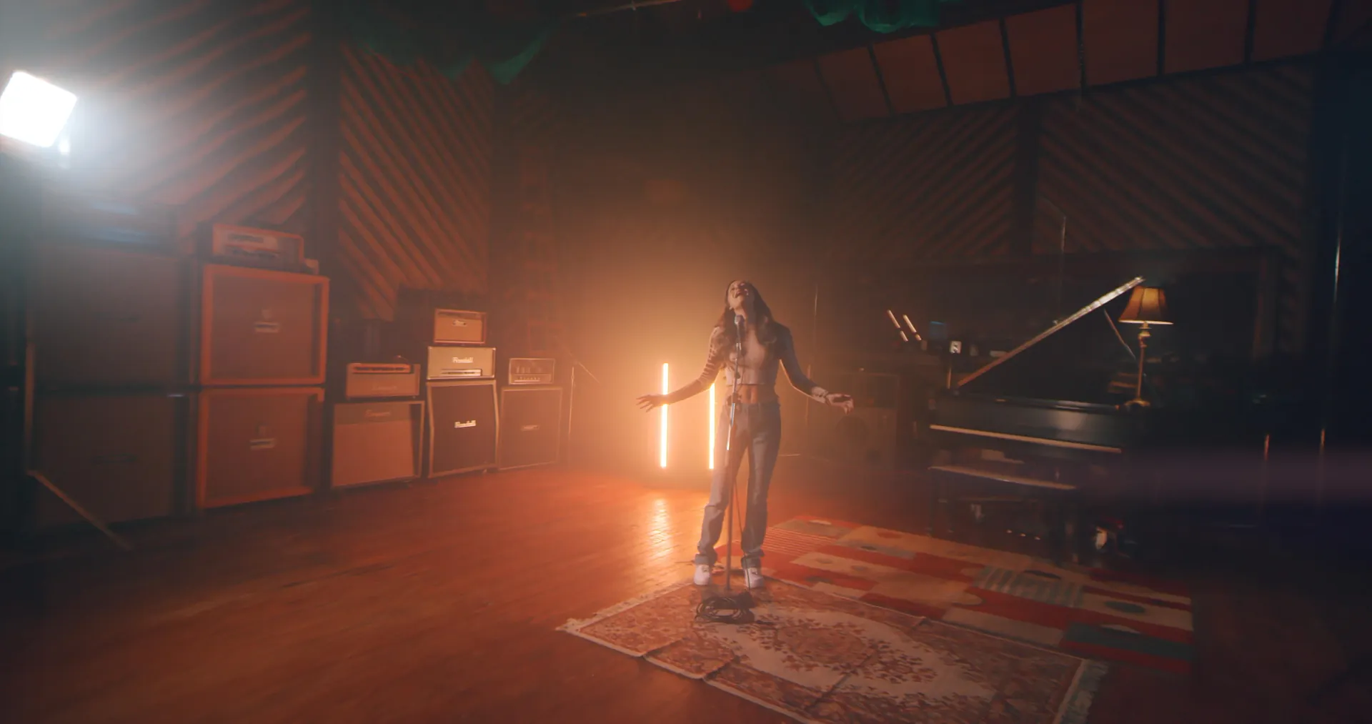 Music video still filmed at Shorefire Recording Studios in Long Branch, NJ: a singer on a rug in the hazy live room, between amp stacks and a grand piano